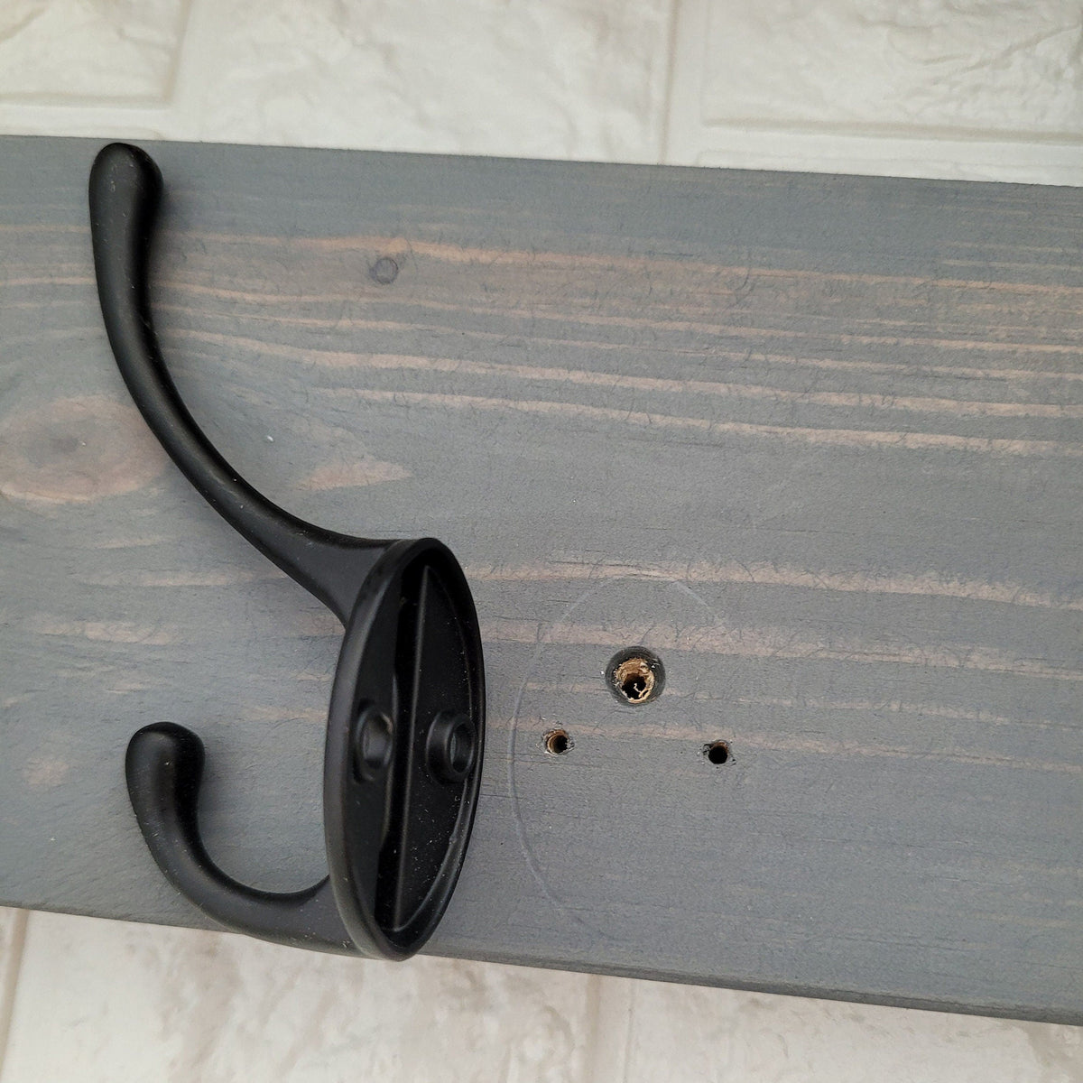 Detail of a single black double hook screwed to the grey painted wood backboard